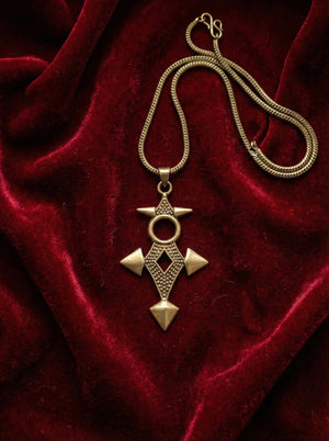 The Scroll Pendant makes a striking geometric statement jewelry piece, its bronze form featuring intricate shapes and resting elegantly on deep red velvet fabric.