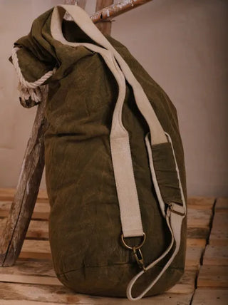 The Vegvisir Duffle bag in large olive-green, featuring a beige strap and rope drawstring, rests on a wooden pallet by a rustic ladder—perfect for secure storage and style on any adventure.