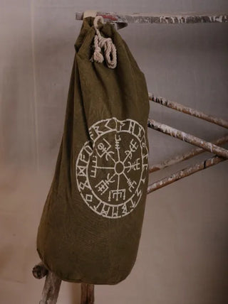 The Vegvisir Duffle Bag, in green, hangs on a rustic wooden ladder. It showcases a white circular Norse compass design with runic symbols—perfect for secure storage and stylish travel.