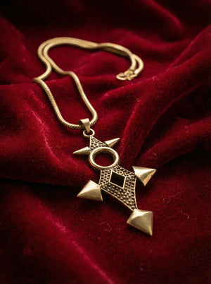 A striking Scroll Pendant in antique gold with geometric designs rests on rich, red velvet fabric, offering a bold take on geometric statement jewelry.