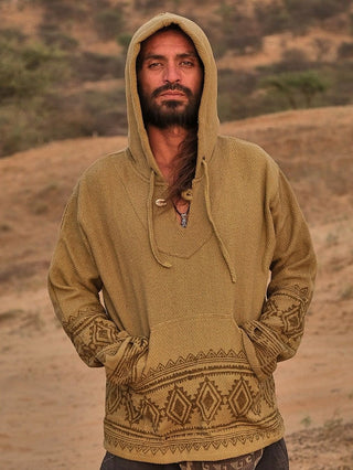 In a desert-like setting, someone wears a sand yellow Tribal Hoodie with intricate patterns. Sandy hills and sparse vegetation enhance the boho babe vibe, while their hands rest comfortably in the hoodies front pocket.