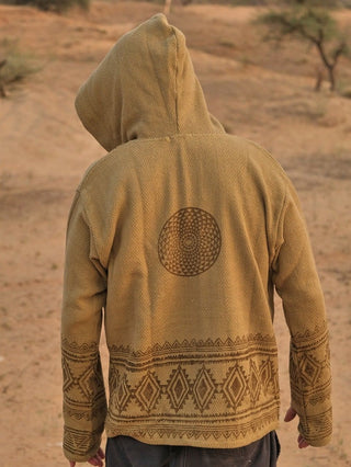 A person wearing the Tribal Hoodie, featuring brown geometric patterns and a circular block print design on the back, stands facing away in a sandy desert landscape with sparse vegetation.