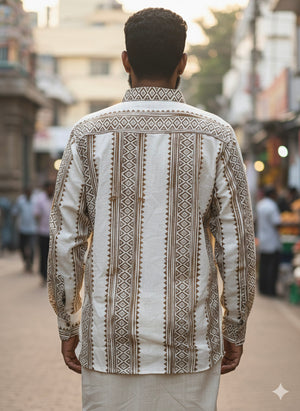 A man stands outdoors with his back to the camera, wearing the artisanal Dwara Shirt in cream and brown, adorned with geometric patterns, paired with a white dhoti. The scene appears to be a busy street.