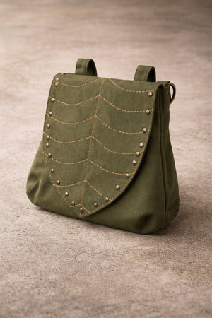 Luna Festival Bag in olive green fabric, designed as a utility sling with a flap featuring curved stitched lines and metal stud accents, displayed on a neutral textured surface.