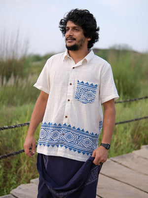 A man with curly hair is wearing the Bohemian Tribal Shirt, which features blue tribal block print patterns on breathable cotton, along with dark pants. He stands on a wooden path outdoors, with green grass in the background.