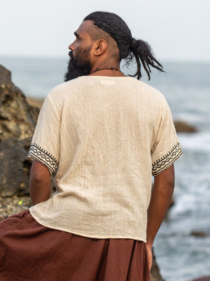 Back view of the model looking out to sea in the cream tribal block print t-shirt, showing the undyed natural cotton back panel and the black hand block printed geometric trim across both short sleeves.