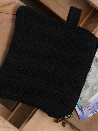 The Upcycled Coin Pouch, made from recycled materials, partially opens to reveal Indian currency notes. This compact black knit pouch rests on a wooden surface, highlighting its eco-friendly charm.