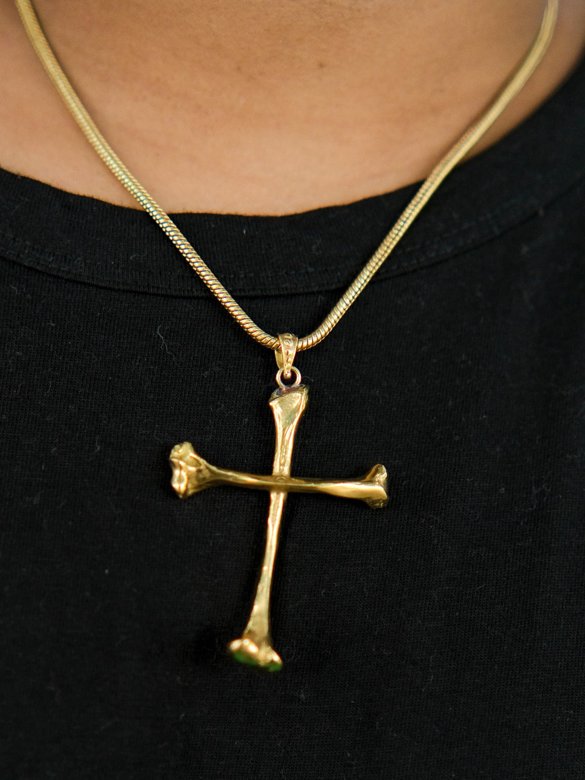 A person wearing a black shirt and the Eternal Relic Necklace, a gothic piece with a gold pendant shaped like two crossed bones.