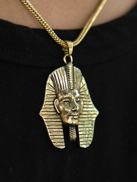 Sure! Here’s a rewritten version using the product name: The Pharaoh Necklace features a gold pendant shaped like an ancient Egyptian pharaoh’s head, adorned with intricate lines and a majestic headdress. Worn over a black shirt, this piece is a striking tribute to traditional Egyptian jewelry.