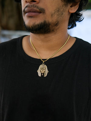 Wearing a black shirt, the person displays their unique taste in Egyptian jewelry with the Pharaoh Necklace, featuring a gold pendant shaped like an ancient Egyptian pharaoh’s mask.