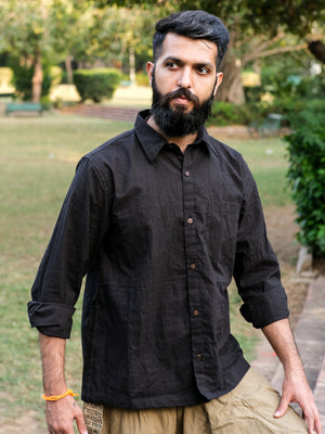 A bearded man with short dark hair stands outdoors in a park with greenery in the background, wearing a Bhadra Shirt made from premium fabric.