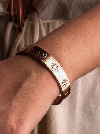 Wearing the shariq Seven Chakra Bracelet with engraved geometric patterns, a person embarks on a spiritual journey. The neutral background softly contrasts, enhancing the metallic sheen and aligning energy centers harmoniously.