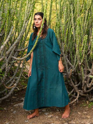 A woman stands barefoot among tall green cacti, wearing an elegant teal Garga Dress with black geometric block printing. Her hair is partly braided as she is surrounded by natural cactus branches.