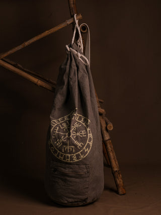 The Vegvisir Duffle bag features a gray design with Norse runes and rests against a bamboo structure on a brown background, making it an ideal companion for secure storage and travel.