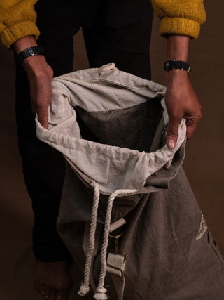 A person with a yellow sweater and wristwatch holds open the spacious Vegvisir Duffle bag, empty and seen from above against a plain brown background—ideal for secure storage on your travels.