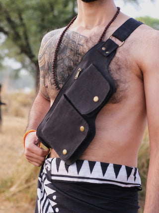 A person outdoors showcases a black Luca Festival Bag and necklace, with a patterned black and white scarf draped around their waist. A tree in the blurred background evokes an unforgettable festival experience.