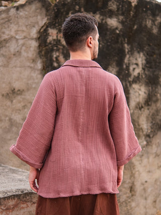 A person stands outdoors with their back to the camera, wearing a loose Yugma Baggy Shirt made from premium quality fabric and brown pants, set against a textured stone or concrete wall.