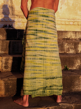 A person stands barefoot on stone steps, basking in warm sunlight with their back and shoulders exposed, wearing the yellow and green striped Leo Dhoti crafted from high-quality materials.