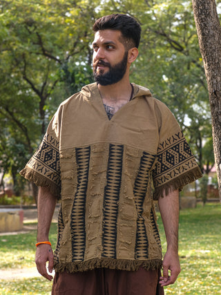 A bearded man stands in a park wearing the Sinai Hoodie, a brown poncho-style top with a bohemian pattern. Trees and grass form the backdrop as he gazes sideways with a slight smile, reminiscent of Rajasthani handblock print styles.