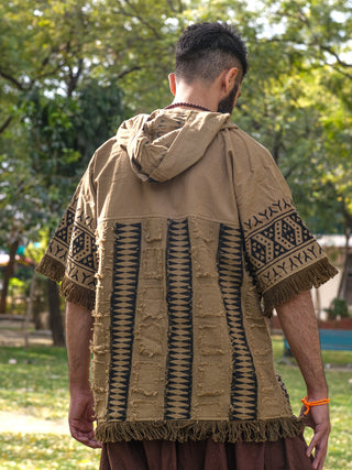 Wearing the Sinai Hoodie with its bohemian fringe and Rajasthani handblock print, a person with short hair stands outdoors facing away. The beige and black colors add flair to the jacket against a backdrop of green trees and grass, creating a serene park atmosphere.