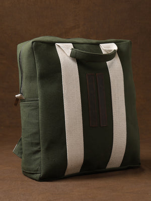The Kelly Back Pack—a green canvas tote with white straps and a zipper—stands upright against a brown background, making it your ideal adventure companion for everyday outings.