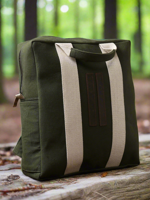 A Kelly Back Pack in green rests stylishly on a wooden surface outdoors, its design making it an ideal adventure companion with the forest softly blurred in the background.