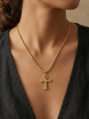 A woman wearing a black V-neck top and a gold Amun Life Key Necklace is photographed from her shoulders to just below her nose. The elegant necklace features the distinctive Egyptian Ankh cross, adding a touch of timeless symbolism to her look.
