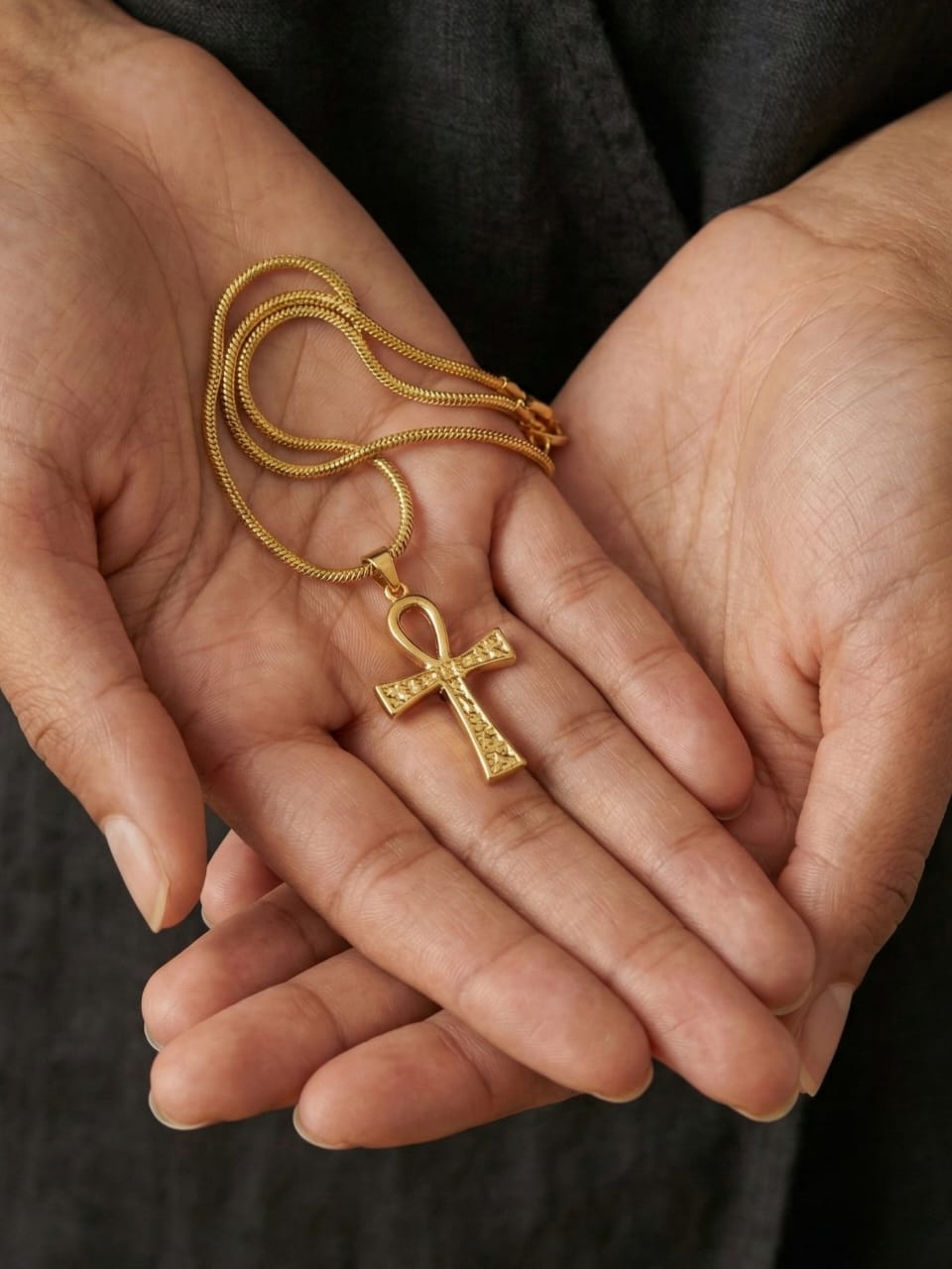 A person holds the Amun Life Key Necklace, featuring an elegant Egyptian Ankh pendant, in their open palms. The background is blurred, emphasizing the striking piece of jewelry.