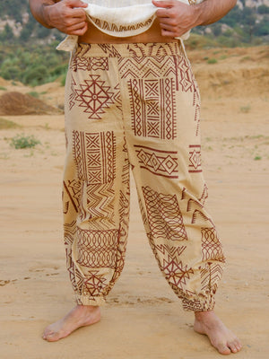 Adivasi unisex harem pants in beige cotton, hand block printed with brown tribal geometric motifs, man holding the waist