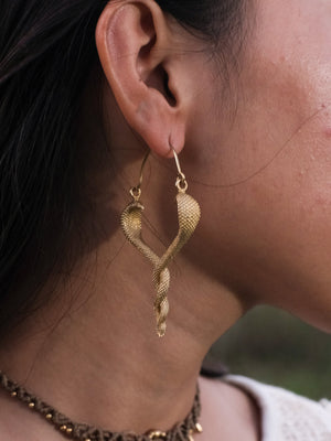 Close-up of the Brahman brass serpent drop earring worn on a model's ear, highlighting the two intertwined snake heads