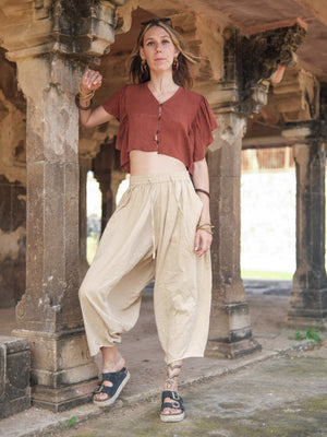 Warm beige cotton harem pants worn full length with a rust cropped top and sandals between carved stone pillars.