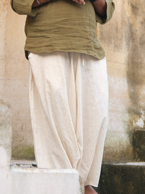 Natural cream harem pants from waist to ankle with an olive tee, standing against a whitewashed wall, legs wide.