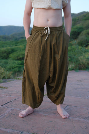 Olive green sirwal harem pants standing barefoot on a terrace, white drawstring cords hanging at the elasticated waist.