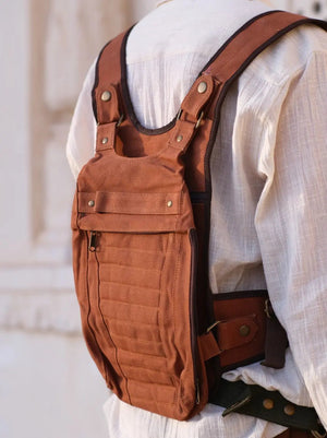 Rust brown harness bag on the back seen from the side, shoulder straps, studs and buckled belt against a wall