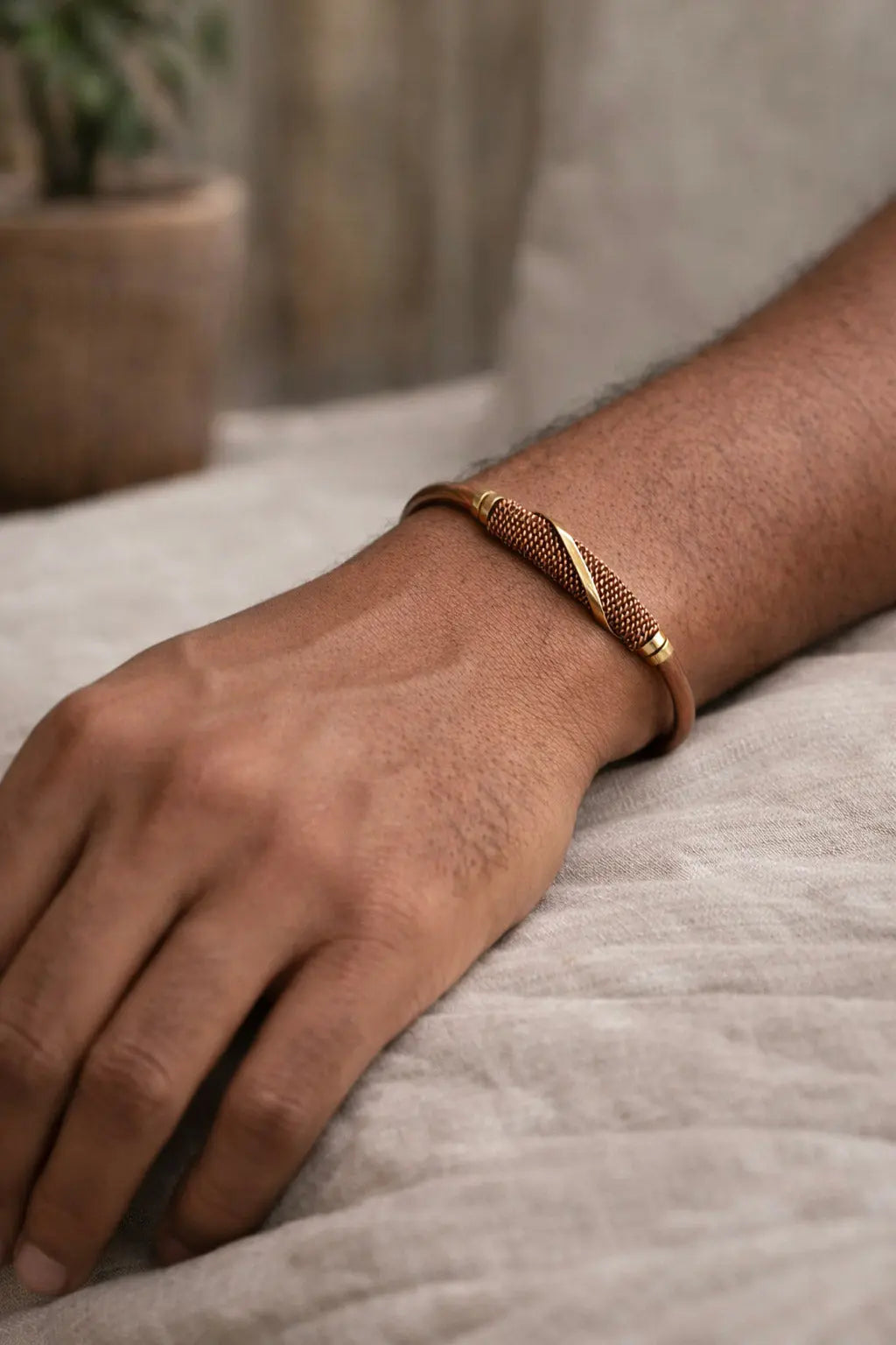 The bronze-toned Kaksha Bracelet, an adjustable cuff featuring a textured, mesh-like center panel, worn on a person’s wrist.