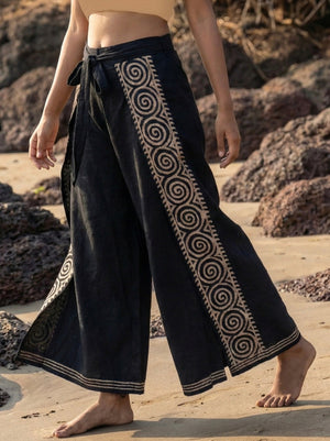 Fisherman wrap pants in black cotton, full body front angled view on beach rocks