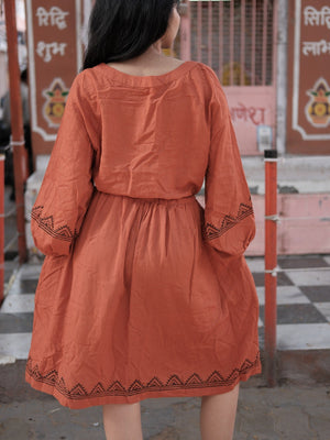 Back view of the Gerua terracotta cotton dress with a gathered waist, embroidered cuffs and a geometric hem border
