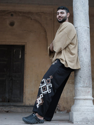 Model leaning on a stone pillar in black Naqsh wide-leg trousers, relaxed cotton streetwear styling