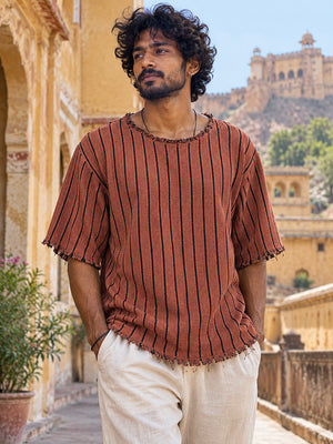 Rang Tee unisex terracotta tee with black vertical stripes and frayed round neckline in a courtyard