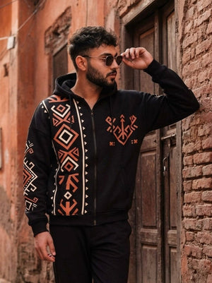 Riwaayat black hoodie with geometric print on a male model wearing sunglasses, three-quarter view