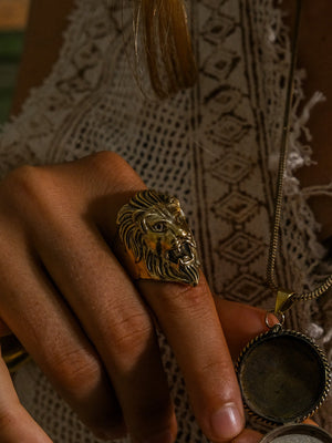 Singam brass lion head ring worn on a finger beside a vintage pendant necklace, showing the antique brass tone