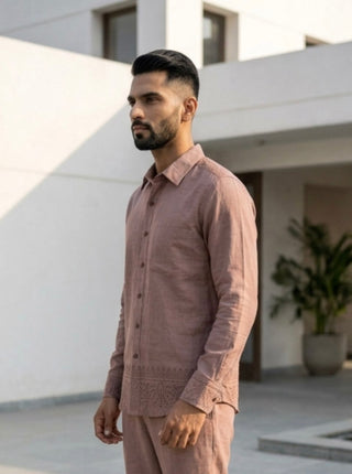 A man with dark hair and a beard stands outdoors, wearing the Madera shirt—a light brown cotton piece featuring hand block print embroidery—paired with matching pants. A modern white building and a potted plant are visible in the background.