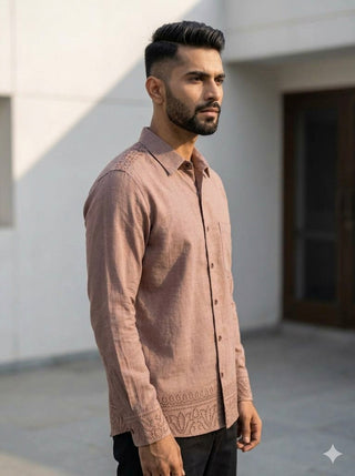 A man with short dark hair and a trimmed beard wears the mauve Madera shirt crafted from breathable cotton with lace detailing. He stands outside on a sunny day near a building, looking to the side with a neutral expression. The comfortable fabric of his Madera shirt complements his understated style.