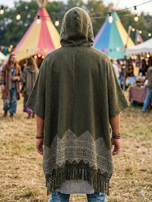 Wearing the Swing Shawl, a person stands outdoors at a festival in front of colorful teepees and string lights, while others in traditional shawls mingle near vibrant booths in the background.