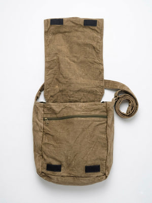 The Vanika Sling Bag is a brown canvas bohemian crossbody featuring artisanal craftsmanship, a long strap, a front zipper pocket, and a flap cover that opens to reveal the interior. The bag appears flat and slightly wrinkled against a plain background.