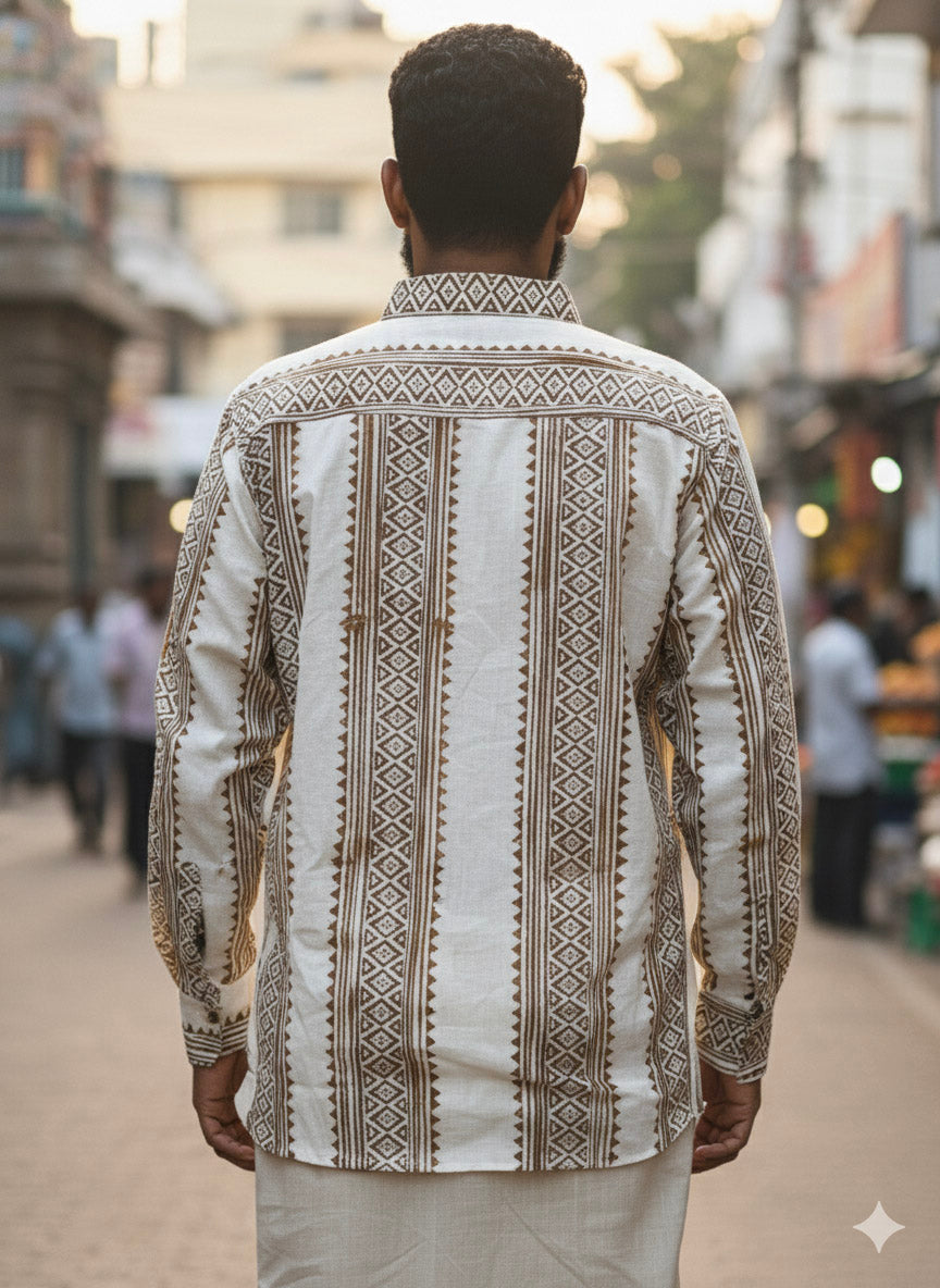A man stands outdoors with his back to the camera, wearing the artisanal Dwara Shirt in cream and brown, adorned with geometric patterns, paired with a white dhoti. The scene appears to be a busy street.