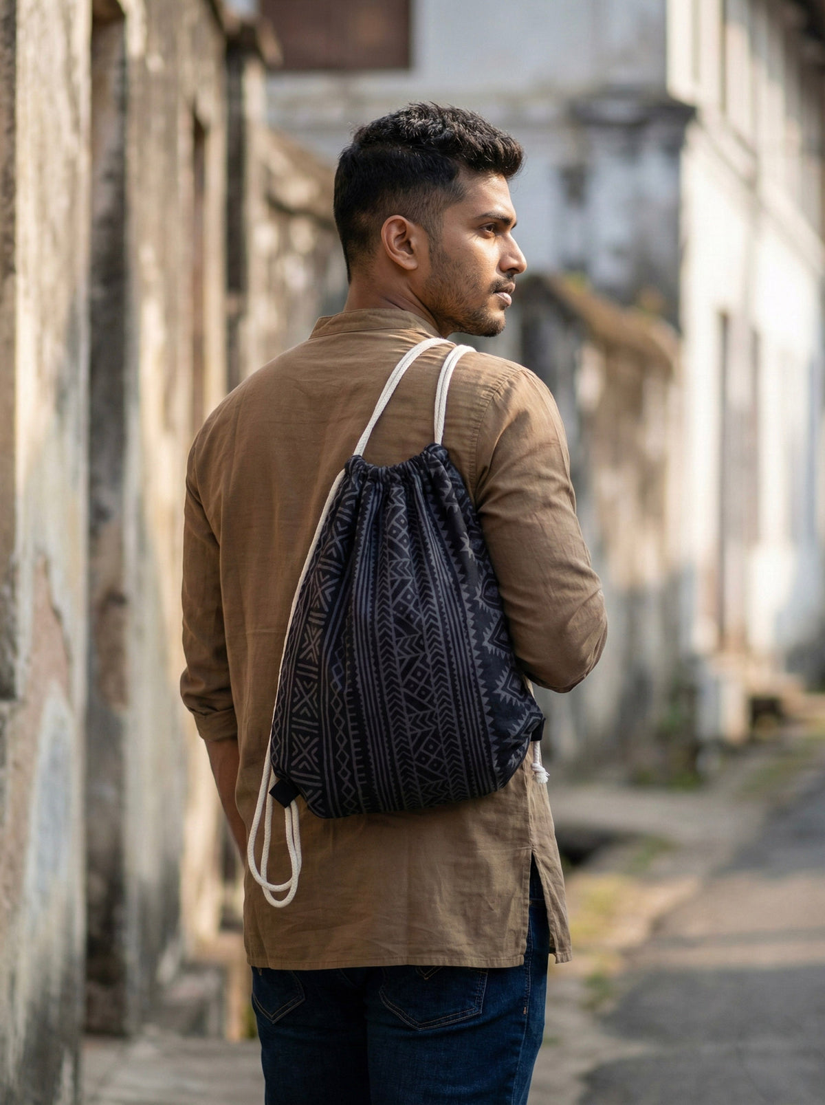 A man wears a black Sahaz Drawstring Bag with a white, hand block-printed tribal pattern on his back.