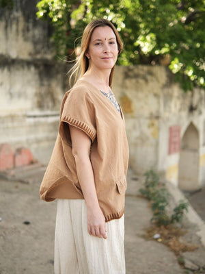 A woman wearing a tan, loose-fitting Mysa Vest in an oversized cotton bohemian style with geometric hem detailing.