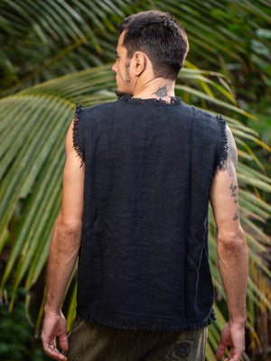 A man stands outdoors with his back to the camera, wearing the Shipibo Tank Top—a sleeveless black textured piece. Palm leaves frame the background, while tattoos are visible on his right arm and neck.