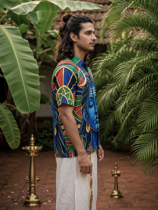 A man with long hair stands sideways outdoors, wearing the Aadi Dev Shirt featuring a blue-faced Shiva-inspired design and white traditional pants, surrounded by lush green plants and brass oil lamps on a tiled floor.